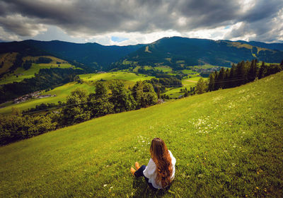 High angle view of woman sitting on grassy mountain