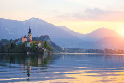 Scenic view of lake by building against sky during sunset