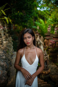 Portrait of young woman standing against trees