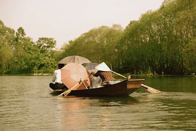 People with umbrellas on boat in mekong river against sky