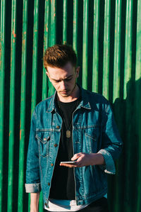 Young man using phone while standing against metal wall