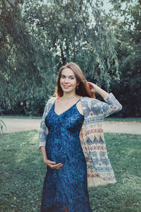 Portrait of smiling pregnant woman standing against trees