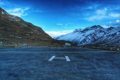 Road sign on snowcapped mountain against blue sky