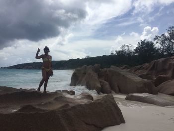 Man standing on rock at beach against sky