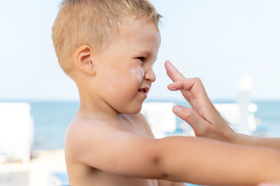 Cropped hand of mother applying suntan lotion to boy