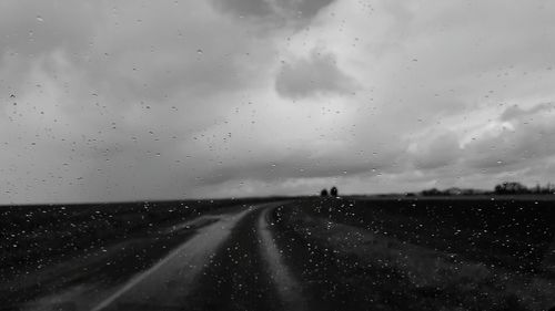 Raindrops on road against sky during sunset