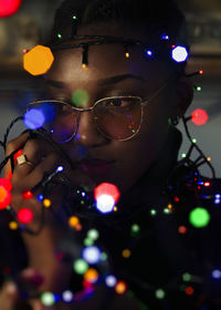 Close-up portrait of young adult wearing sunglasses illuminated with christmas lights 
