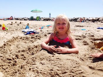 Cute smiling girl buried in sand at beach during summer
