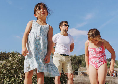 Portrait of father with two daughters standing against sky