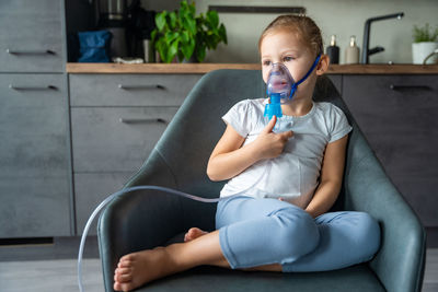 Young woman drinking water while sitting on sofa at home