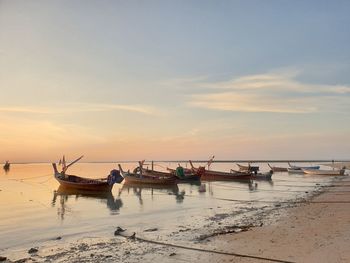 Fishing boats on beach against sky during sunset