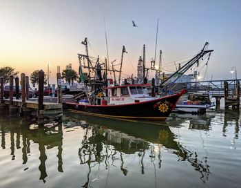 Boats moored in harbor at sunset