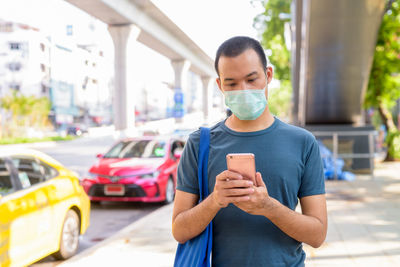 Young man using phone while standing on street in city