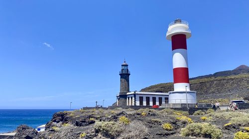 Lighthouse by sea against clear blue sky