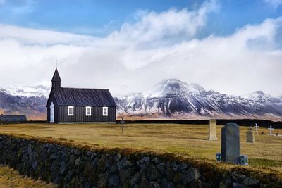 House on field by mountain against sky