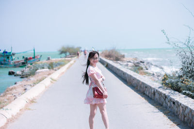 Portrait of woman standing on land by sea against sky