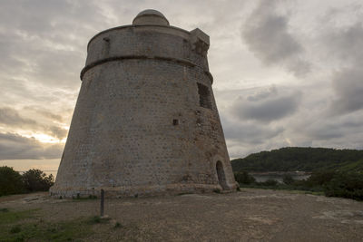 Low angle view of old tower amidst field against sky