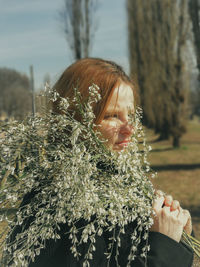 Side view of mature woman holding flowers while standing in park