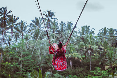 Rear view of woman on swing against sky