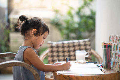 Cute little girl drawing homework and writing with pencil on paper at home
