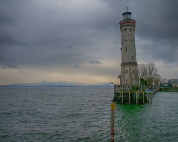 Lighthouse in sea against cloudy sky