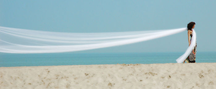 Panoramic view of woman with long white textile walking at beach