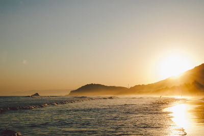 Scenic view of sea by mountain against clear sky during sunset