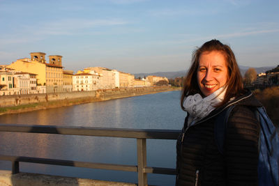 Portrait of smiling woman standing by railing against river in city