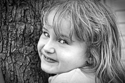 Close-up portrait of cute girl by tree trunk