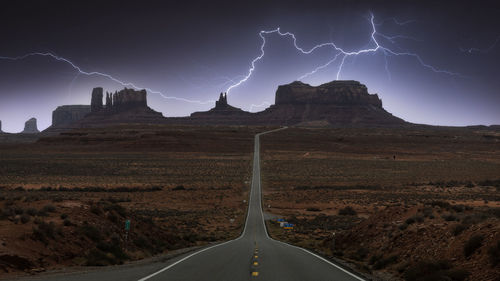 Breathtaking scenery of butte rocky outcrop formations under thunderstorm sky with clouds in between asphalt highway in monument valley navajo tribal park, utah arizona in usa