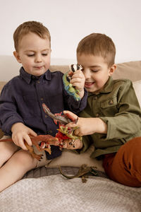 Two little and cute caucasian boys playing with dinosaurs at home.