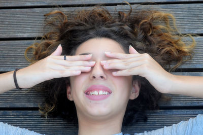 Directly above shot of girl covering her eyes while lying on floorboard