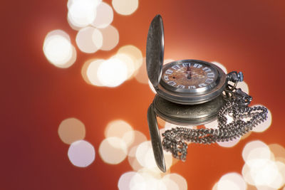 Close-up of pocket watch with illuminated lights in background