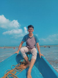 Portrait of young man sitting on boat in sea against sky