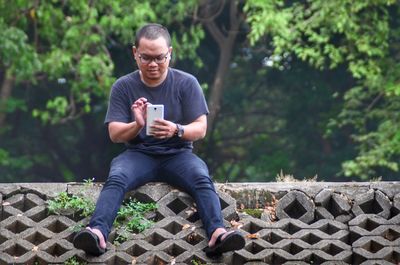 Full length of man sitting on mobile phone in park