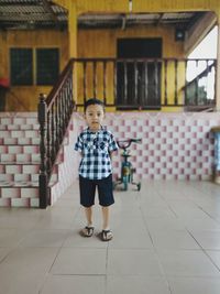 Portrait of cute boy standing on tiled floor against house