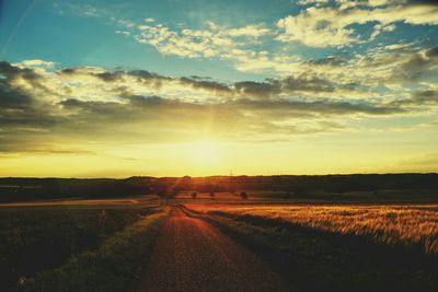 Road amidst field against sky during sunset