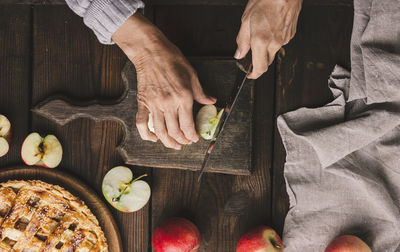 Woman cutting apples for pie on brown wooden table, top view
