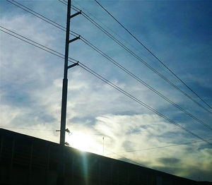 Low angle view of power lines against cloudy sky