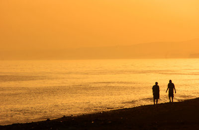 Silhouette people on beach against sky during sunset