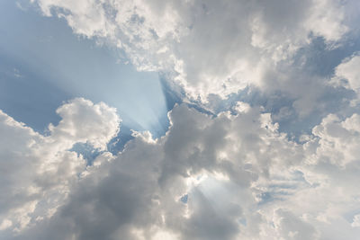 Low angle view of sunlight streaming through clouds