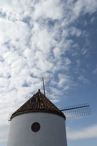 Low angle view of traditional windmill against cloudy sky