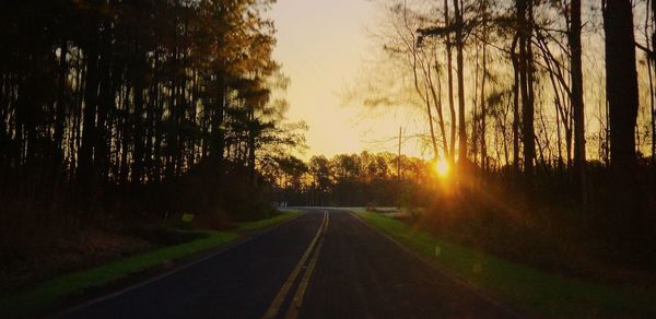 Road amidst trees against sky during sunset