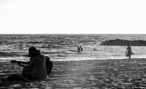 Man sitting on beach against clear sky