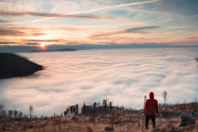 Man aged 20-25 and a red jacket stands on slopes of mount ondrejnik and looks at sunset on radhost