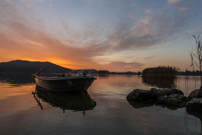 Boats moored in lake against sky during sunset