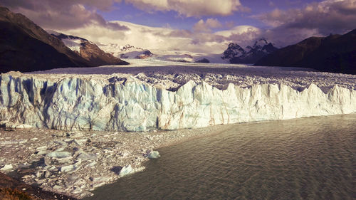 Scenic view of glacier by lake against cloudy sky