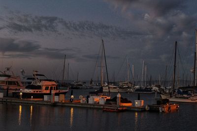 Sailboats moored at harbor against sky at dusk