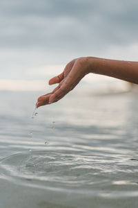 Person hand by sea against sky