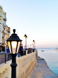 Illuminated street light at beach against clear sky during sunset